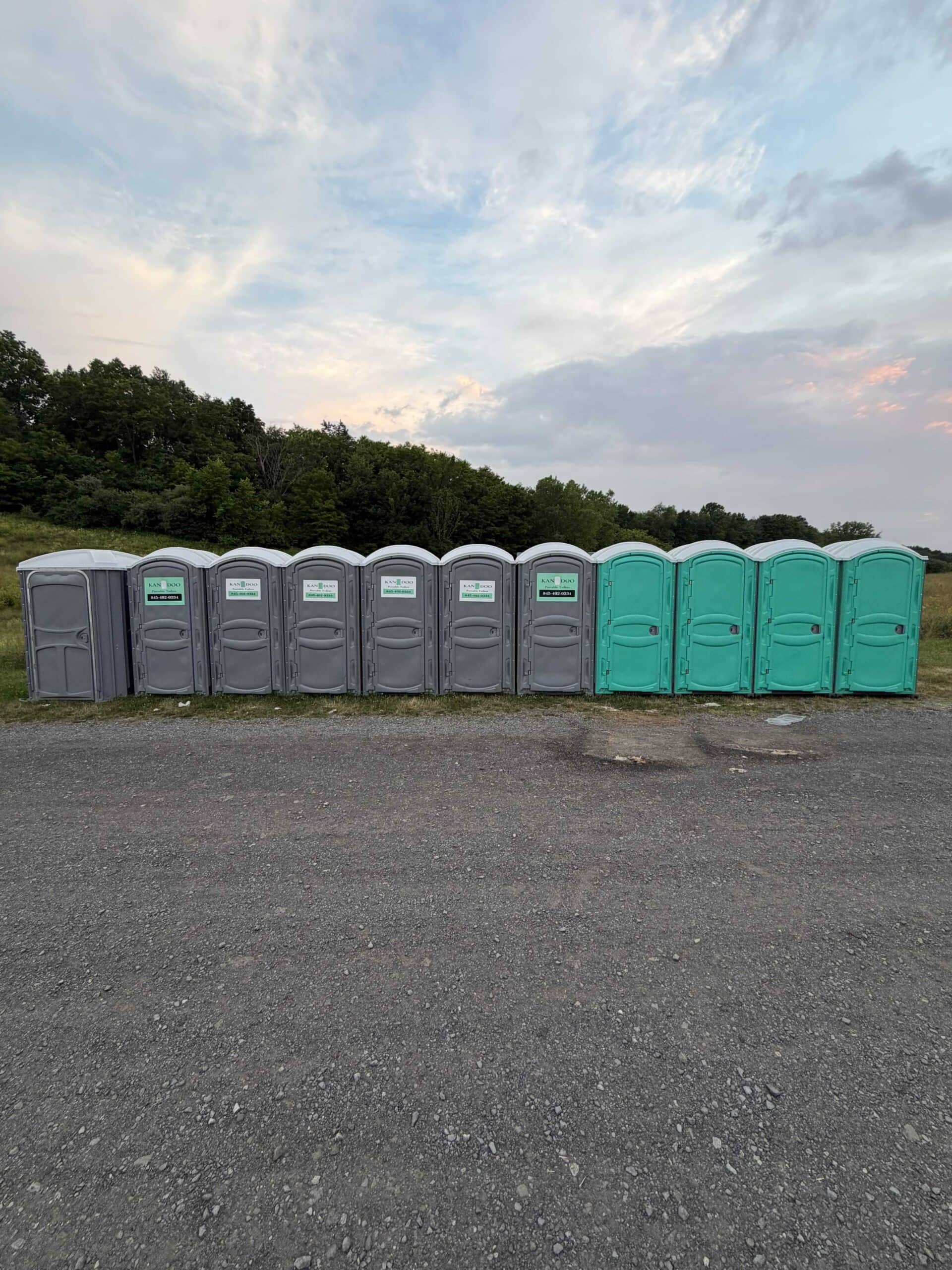 Row of portable toilets in various colors at outdoor event site.